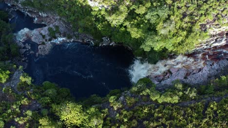 Aerial-drone-wide-bird's-eye-rising-shot-of-the-stunning-Devil's-Pit-waterfall-surrounded-by-rocks-and-jungle-foliage-in-the-beautiful-Chapada-Diamantina-National-Park-in-Northeastern-Brazil