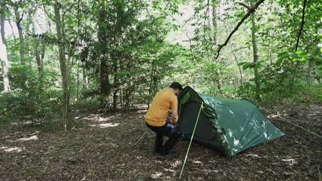 Lonely-camper-walking-into-his-tent-in-dense-woodland-area,-follow-up-view