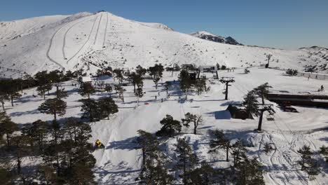 Aerial-view-of-a-ski-station-on-top-of-the-hill-revealing-the-snowy-mountains-behind