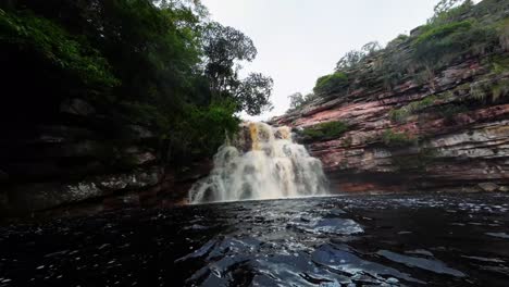 Extreme-wide-action-camera-shot-swimming-inside-of-the-stunning-Devil's-Pit-lake-with-a-large-waterfall-in-the-beautiful-Chapada-Diamantina-National-Park-in-Northeastern-Brazil-on-an-overcast-day