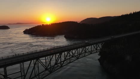 Hero-shot-of-cars-driving-across-Deception-Pass-Bridge-with-the-sun-setting-in-the-background