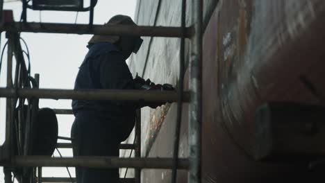 handheld-shot-of-man-on-riser-welding-a-cargo-ship-repairs-in-shipyard-repair