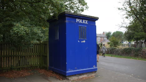 People-walking-past-a-blue-emergency-police-box-at-a-park