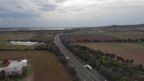 Aerial-Drone-Reverse-Showing-Of-Busy-Hungarian-Highway,-Beautiful-Lake-In-The-Background