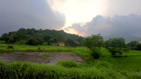 Eine-Schöne-Aussicht-Auf-Einen-Berg-In-Der-Nähe-Eines-Kleinen-Dorfes-Und-Einer-Farm-Und-Eines-Kleinen-Sees-|-Schöner-Grüner-Wald-In-Maharashtra,-Indischer-Monsunzeithintergrund-Mit-Stürmischer-Wolkenlandschaft