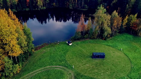 Camping-trailer-and-sauna-by-a-picturesque-lake-in-autumn---aerial-parallax-reveal