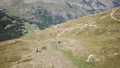 Grassery-field,-mountain-valley-in-the-Swiss-alps,-drone-aerial-view-on-hikers,-walkers-doing-a-lunch-break-during-a-sport-activity-in-the-mountain