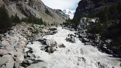 Torrente-Fangoso-En-Un-Valle-De-Los-Alpes-Suizos-Junto-A-Las-Cumbres-De-Las-Montañas-Rocosas,-El-Glaciar-Se-Derrite-Debido-Al-Calentamiento-Global