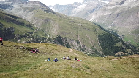 Los-Caminantes-Toman-Su-Descanso-Con-Una-Hermosa-Vista-De-Los-Alpes-Suizos,-Prados-Con-Hierba,-Cumbres-Rocosas-De-Zermatt,-Paisaje-Natural,-Antena-De-Drones