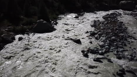 Muddy-and-rocky-river,-stream-in-the-Swiss-alps-mountain,-water-from-the-glacier,-drone-aerial-view