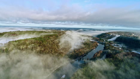Low-valley-fog-along-a-river-through-a-picturesque-mountain-forest---pull-back-aerial-view