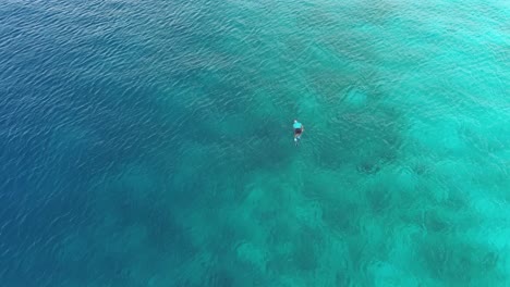 man-snorkeling-alone-in-clear-blue-ocean-water-drone-view-from-above-deepwater-and-mountains-in-background