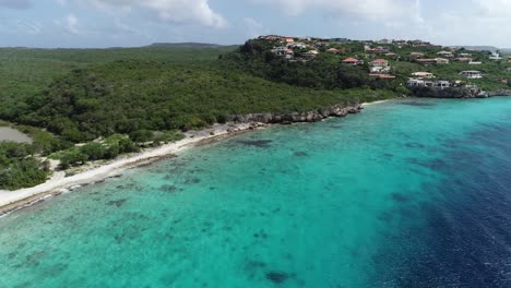 drone-flying-away-from-island-with-clear-ocean-water-and-greenery