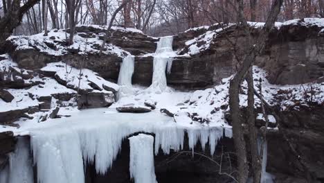 Drone-descending-shot-of-a-frozen-waterfall-in-Minnesota,-Triple-falls