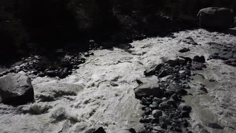 Drohnenluftaufnahme-Eines-Flusses-In-Den-Schweizer-Alpen-Mit-Starker-Strömung,-Die-Das-Wasser-Schlammig-Macht-Und-Felsen-Auf-Dem-Flussbett
