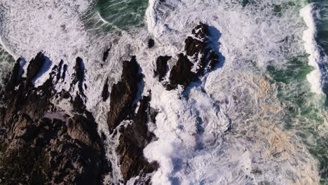 Aerial-Riser-über-Wellen,-Die-Spektakulär-Gegen-Die-Zerklüftete-Küste-Krachen