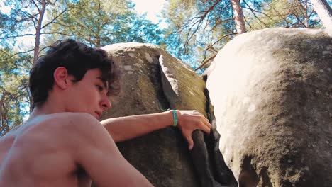 upper-body-of-a-teenage-boy-climbing-a-crack-in-boulder-in-fontainebleau-summer
