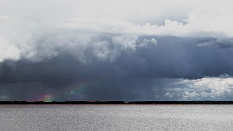 Static-timelapse-of-rain-clouds-and-rainbow-over-sea-and-distant-coast