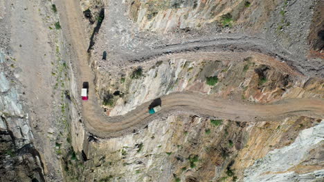 Breathtaking-drone-shot-of-tow-vehicles-coming-up-to-a-bend-on-Fairy-Meadows-Road-in-Pakistan,-second-deadliest-highway-in-the-world,-downward-angle-aerial-shot