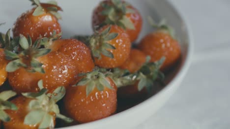 Detail-of-a-white-bowl-of-delicious-red-strawberries,-a-hand-reaches-in-and-takes-one