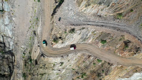 Dramatic-drone-shot-of-vehicles-passing-each-other-on-Fairy-Meadows-Road-in-Pakistan,-second-deadliest-highway-in-the-world,-downward-angle-aerial