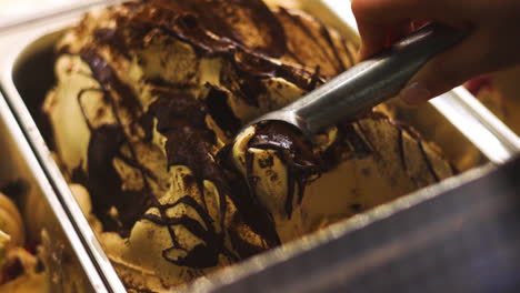 Manicured-female-hand-scooping-chocolate-hazelnut-ice-cream-out-of-gelato-pan