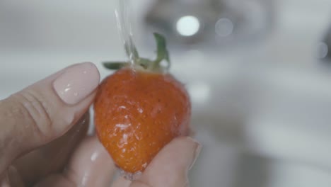 A-strawberry-is-held-and-carefully-washed-under-water-in-slow-motion