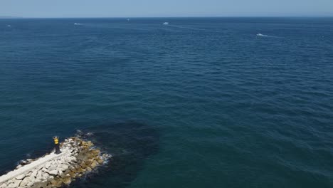 Boat-signal-tower-on-end-of-breakwater-near-blue-ocean-water,-aerial-view