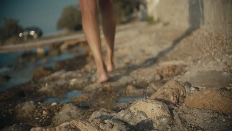 Low-angle-of-woman-shoeless-legs-walking-on-stony-beach