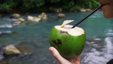Beber-Jugo-De-Agua-De-Coco-Saludable-En-La-Selva-Tropical-Con-Pajita-De-Plástico-En-Río-Celeste,-Costa-Rica