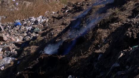 Slow-motion,-handheld-view-of-smoke-and-flames-emerging-from-the-garbage-at-a-dumping-site
