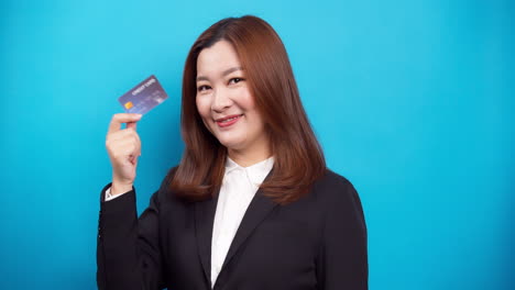 Schöne-Asiatische-Geschäftsfrau-Im-Schwarzen-Anzug,-Die-Kreditkarte-Mit-Einem-Lächeln-Im-Studio-Auf-Blauem-Hintergrund-Hält