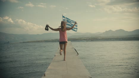 Woman-shoeless-dancing-sirtaki-on-sea-pier-in-front-of-a-Greek-flag