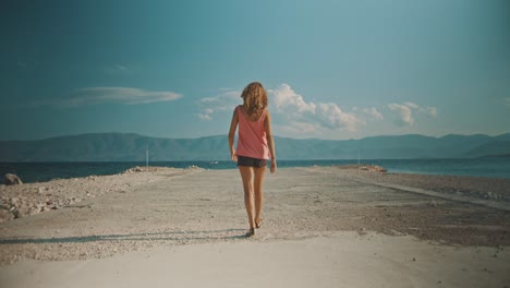 Woman-walking-on-a-concrete-jetty-towards-to-the-sea-water