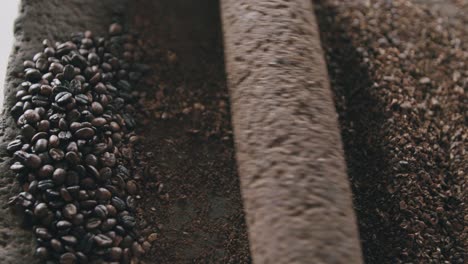 Slow-motion-top-view-of-person-slowly-grinding-coffee-beans-with-a-rock-roller-on-a-volcanic-stone
