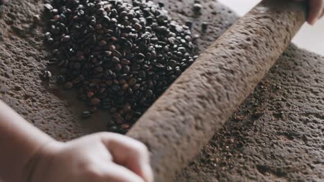 Slow-motion-footage-of-person-just-starting-to-grind-coffee-beans-on-a-volcanic-stone-with-a-stone-roll-pin