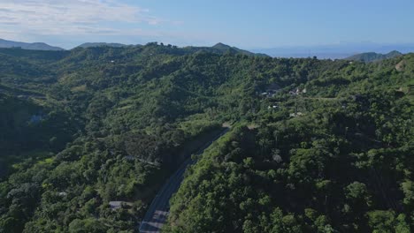 Drone-flight-over-hill-road-with-traffic-between-green-mountains-in-Puerto-Plata,Dominican-Republic