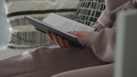 Woman-is-reading-a-book-on-the-sofa,-flipping-pages,-cozy-home-atmosphere