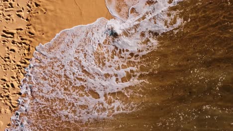 Fabelhafter-Schuss-Einer-Welle,-Die-über-Einen-Fußabdruck-Im-Sand-Kommt-Und-Ihn-Löscht,-Ericeira-Portugal
