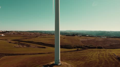 Tiro-De-Gran-Altura-De-Una-Gran-Turbina-Eólica-Con-Un-Impresionante-Paisaje-Verde,-Ericeira,-Portugal