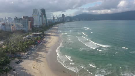 Aerial-view-of-long-white-sand-stretch-My-Khe,-My-Bac-An-and-Non-Nuoc-beach-with-mountains-and-waves-on-sunny-day-in-Danang,-Central-Vietnam