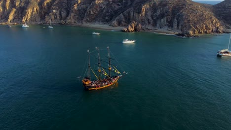 Pirate-ship-in-the-middle-of-the-sea,-near-some-mountains-at-sunset