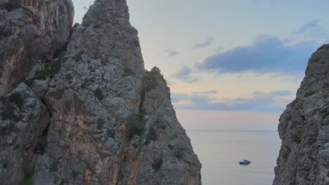 Sideways-drone-shot-revealing-Mediterranean-sea-and-boats-behind-pointy-rock-formations-at-Sa-Calobra,-Mallorca,-Spain