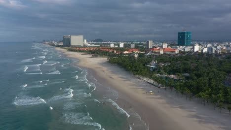 Drone-flying-over-famous-My-Khe,-My-Bac-An-and-Non-Nuoc-white-sand-beach-with-huge-waves-in-Danang,-Central-Vietnam