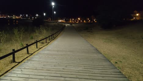 Gruppe-Junger-Leute,-Die-Auf-Der-In-Der-Nacht-Von-Laternen-Beleuchteten-Holzbrücke-Spazieren-Gehen