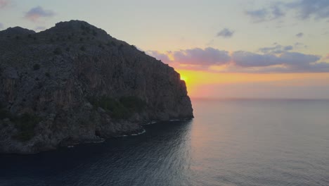 Sideways-revealing-drone-shot-of-the-sunset-at-Sa-Calobra,-Mallorca,-Spain-behind-a-big-mountain-above-the-Mediterranean-sea