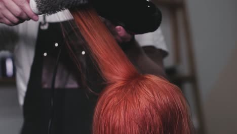 Hairstylist-blow-drying-the-red-hair-of-a-female-client-in-a-hair-saloon