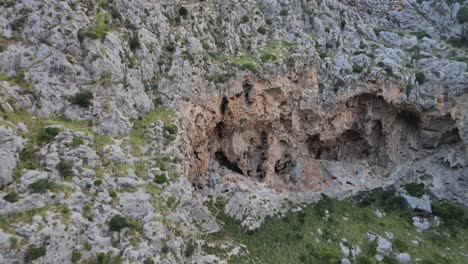 Flying-towards-a-mountain-side-with-holes-in-them-at-the-canyon-of-Sa-Calobra,-Mallorca,-Spain