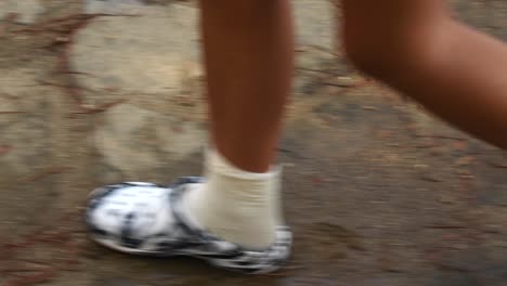 Side-view-of-woman-legs-in-white-flip-flops-walking-in-wet-floor-in-the-forest
