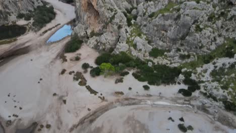 Tilting-drone-shot-of-a-canyon-with-water-at-the-bottom-at-Sa-Calobra,-Mallorca,-Spain